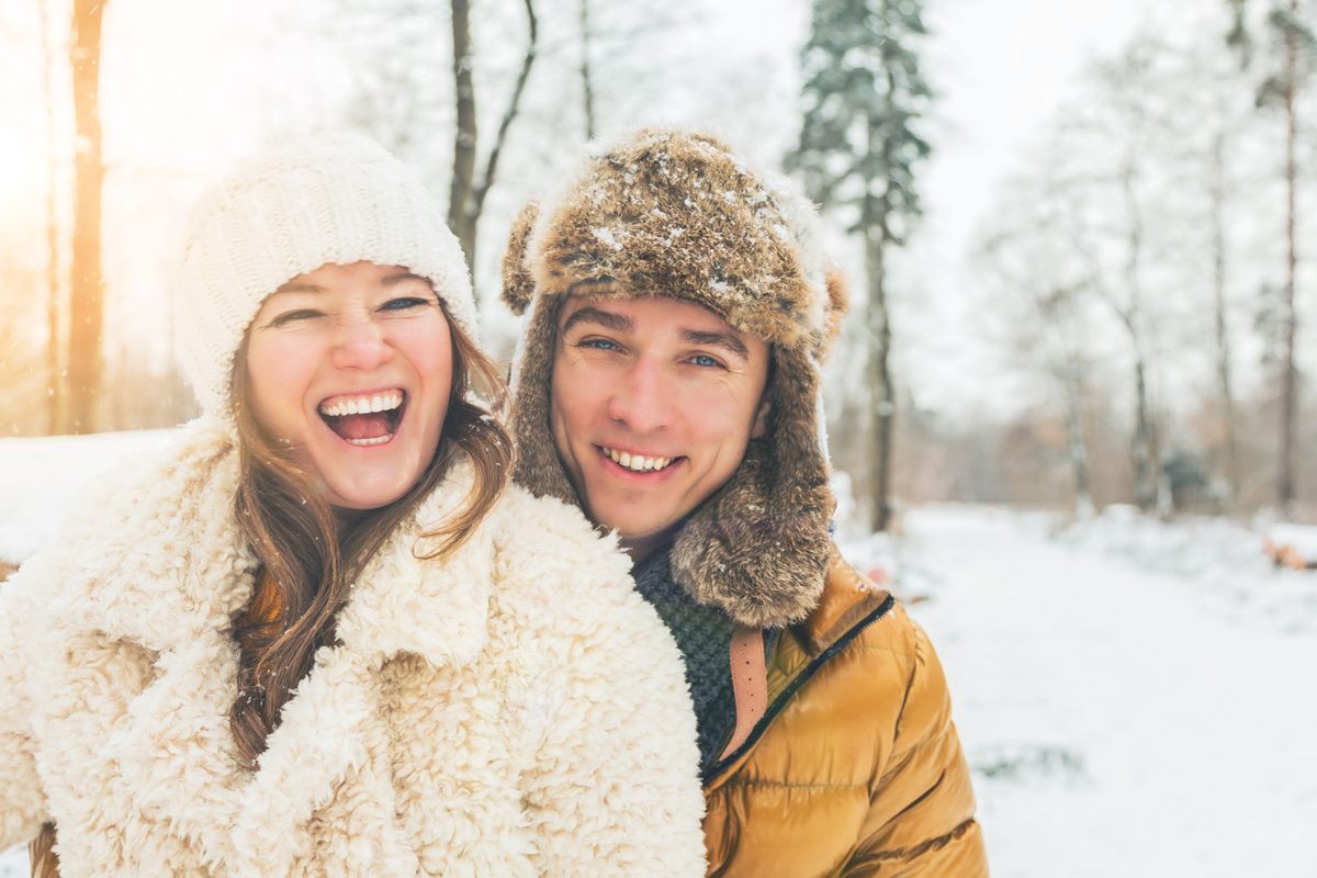 Two people laughing together in the snow on a bright winter day